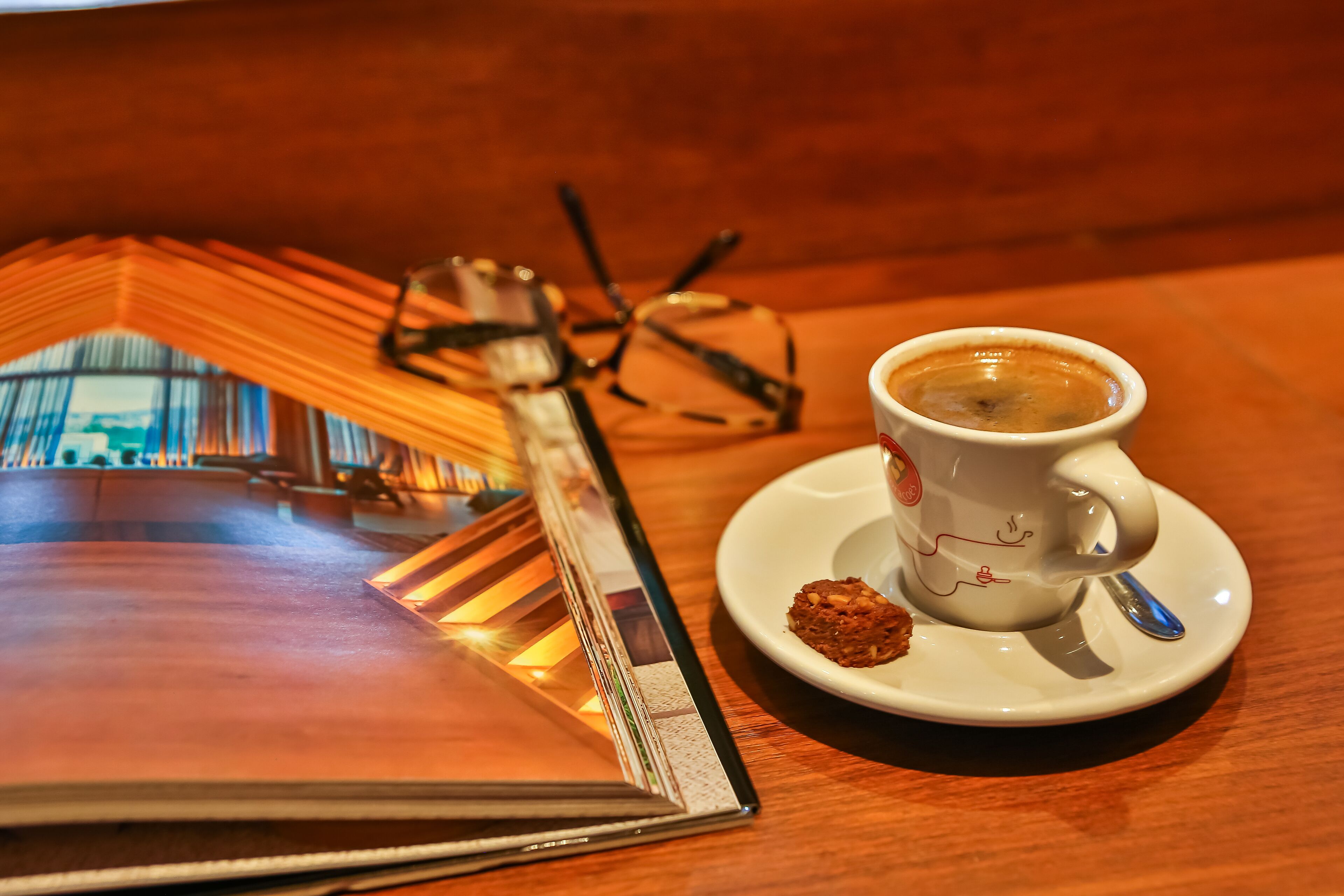 A table with a cup of coffee, a muffin, and a pair of glasses.