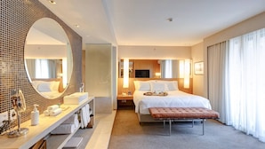 A modern hotel room with a large mirror, a bed with white linens, a bedside table with a lamp, and a large window with curtains. - Radisson Blu São Paulo (São Paulo)
