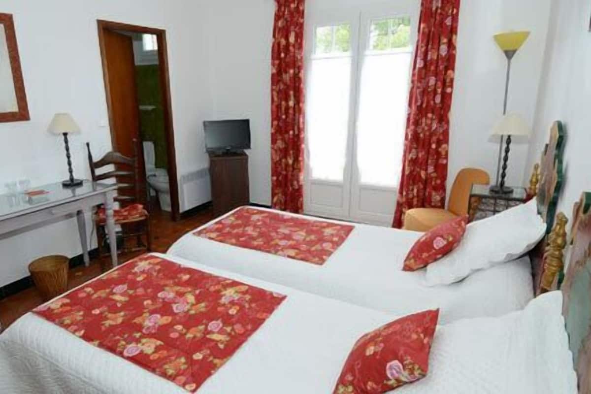 A hotel room with two beds, a desk, a chair, a television, and a lamp.