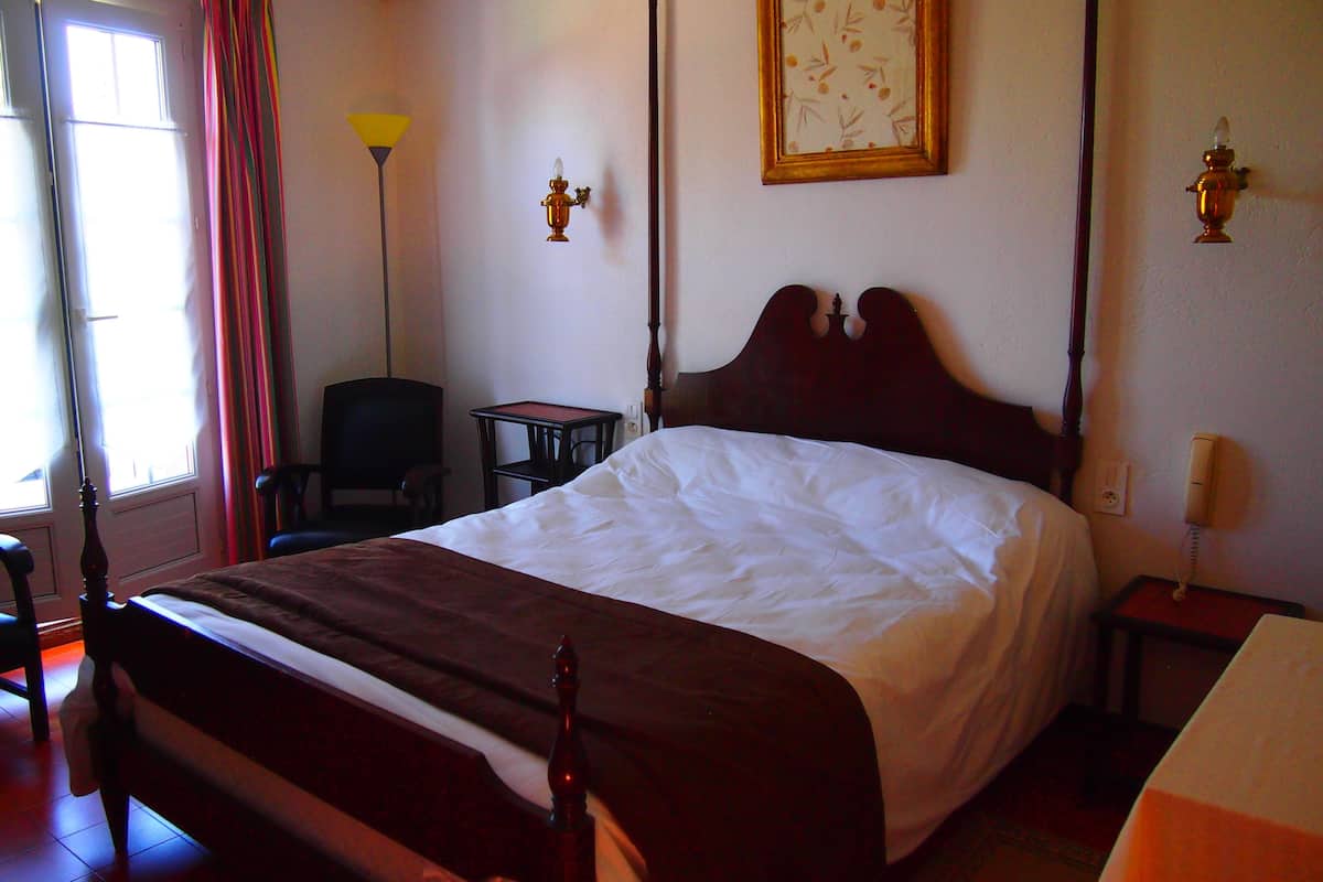 A hotel room with a large bed, a chair, a desk, and a lamp.