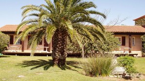 A palm tree in front of a building with a tiled roof and outdoor seating. - Le Relais du Val d'Orbieu (Ornaisons)