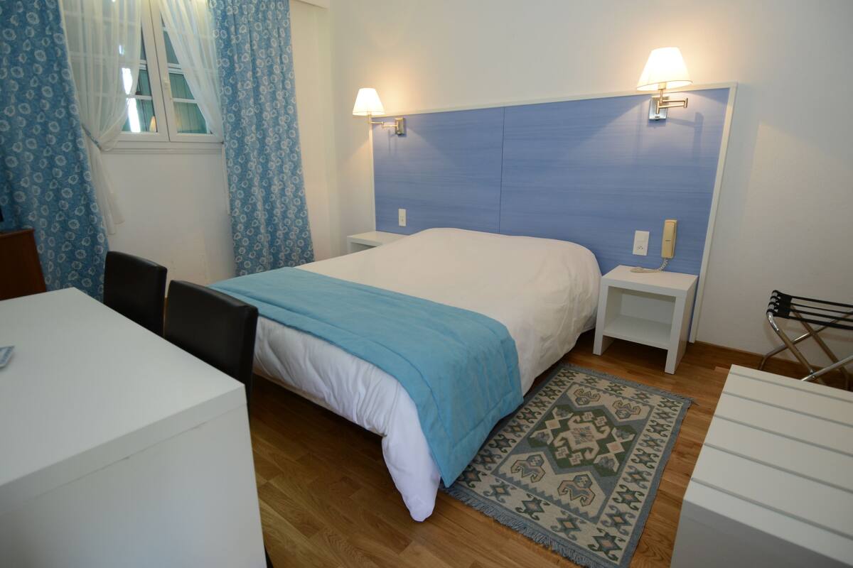 A hotel room with a bed, bedside tables, a desk, and a chair.