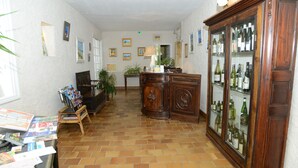 A hallway with a tiled floor, a wooden cabinet with glass doors, and a small table with books and magazines. - Le Relais du Val d'Orbieu (Ornaisons)