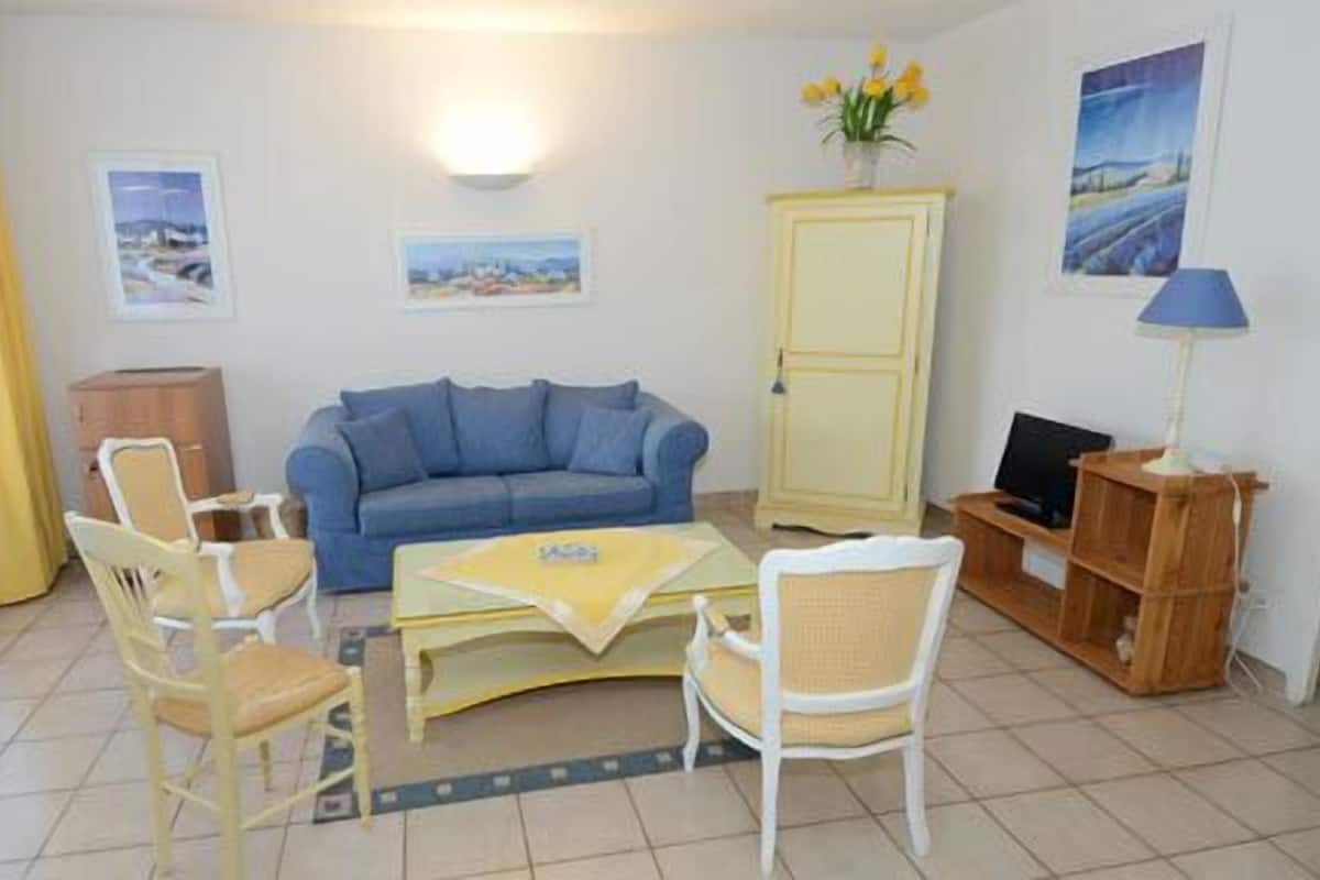 A living room with a blue sofa, two white chairs, a yellow coffee table, a wooden cabinet, and a TV stand.