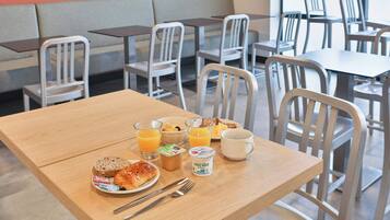 Una mesa de desayuno con un plato de comida, un vaso de jugo de naranja, una taza y un recipiente de yogurt.