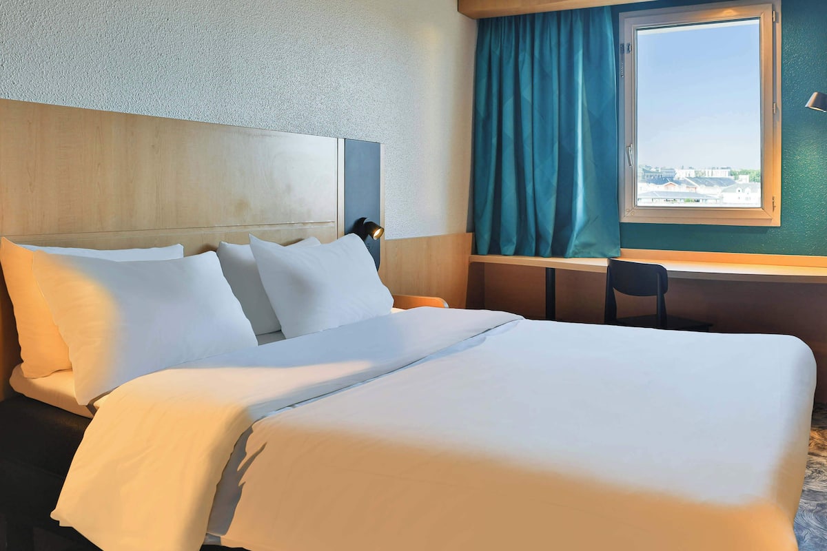 Une chambre d’hôtel avec un grand lit, un bureau et une fenêtre avec des rideaux.