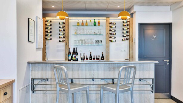 Zona de bar con dos taburetes, estantes con botellas y vasos, y una puerta con la leyenda 'Local privé'.