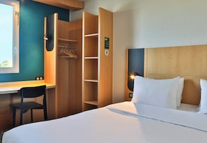 Ein Hotelzimmer mit Bett, Schreibtisch, Stuhl, Kleiderschrank und Blick ins Freie.