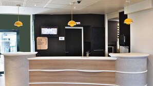 Un mostrador de recepción de diseño moderno, con acabado de madera y forma curvada. Dos lámparas colgantes están suspendidas sobre el mostrador, y una pantalla digital muestra información en la pared de fondo.