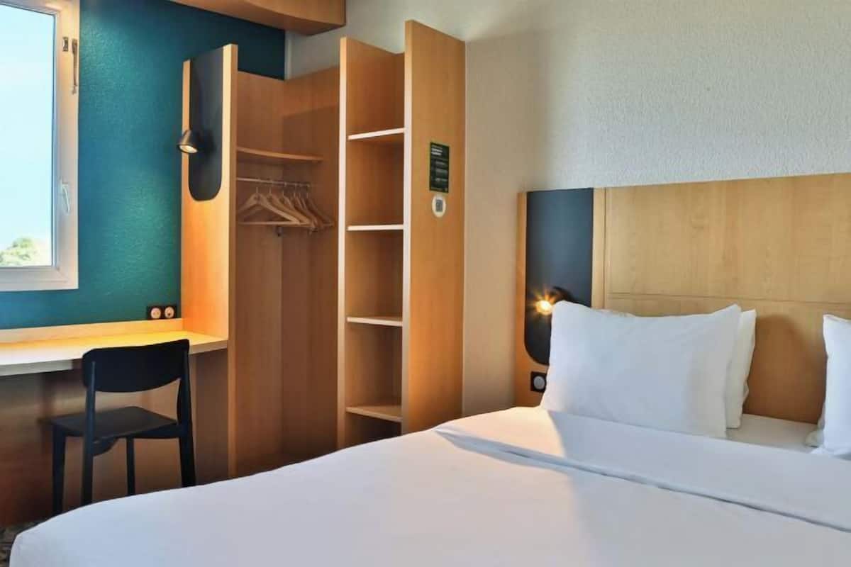 Une chambre d’hôtel comprenant un lit, un bureau, une chaise, une armoire et une table de chevet.