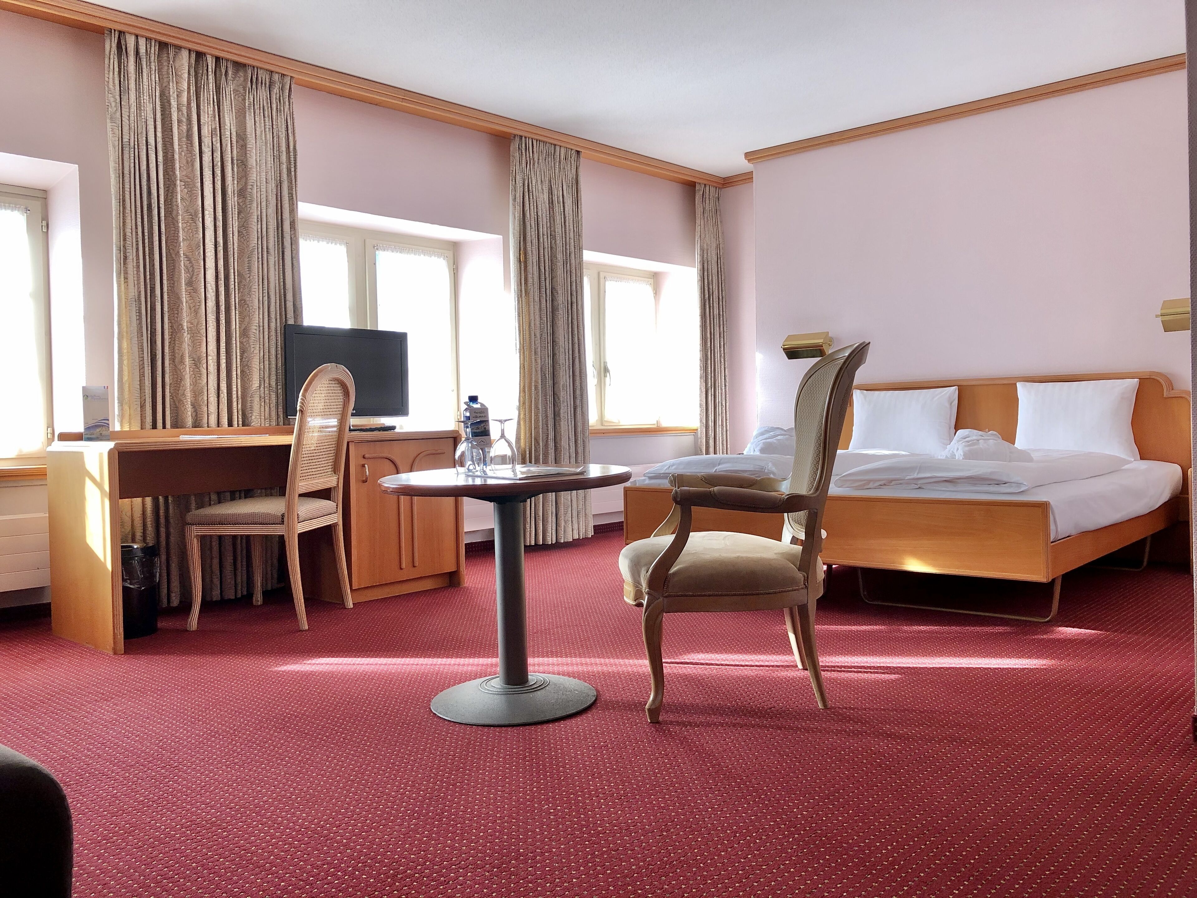 A hotel room with a bed, a desk, a chair, a television, and a window with curtains.
