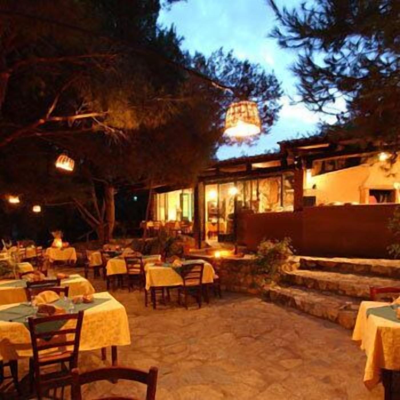 Un espacio exterior para comer con mesas y sillas, un sendero de piedra y un edificio con grandes ventanales.