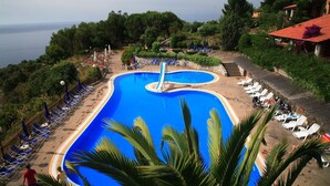 A large, curved swimming pool with a slide, surrounded by lounge chairs and umbrellas, overlooking a body of water. - King's Residence Hotel (Centola)