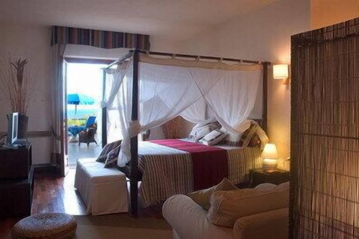 Una camera da letto con un letto a baldacchino, un comodino con una lampada, un divano e vista sull'esterno.