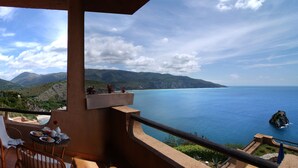 A balcony with a view of the sea and mountains, a table with breakfast items, and a chair. - King's Residence Hotel (Centola)