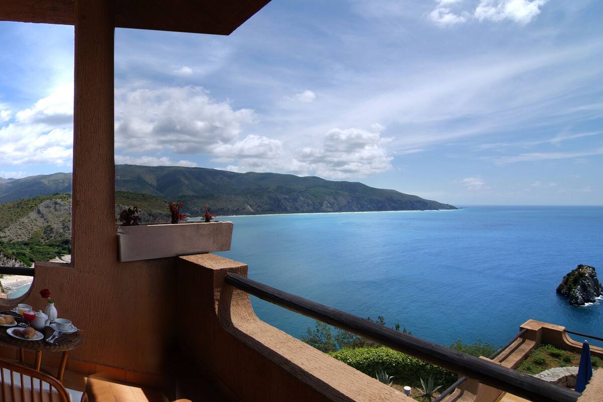 Un balcone con vista sul mare e sulle montagne, un tavolo con prodotti per la colazione e una sedia.