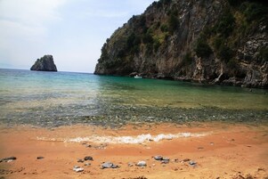Una playa con agua cristalina, un promontorio rocoso y una isla en la distancia.