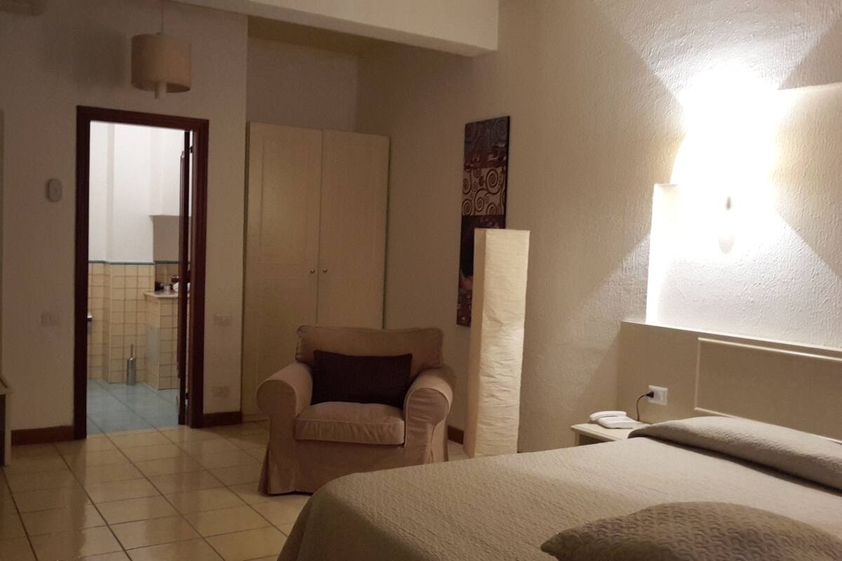 Una camera d'hotel con un letto, una sedia, un armadio e un bagno visibile attraverso una porta aperta.