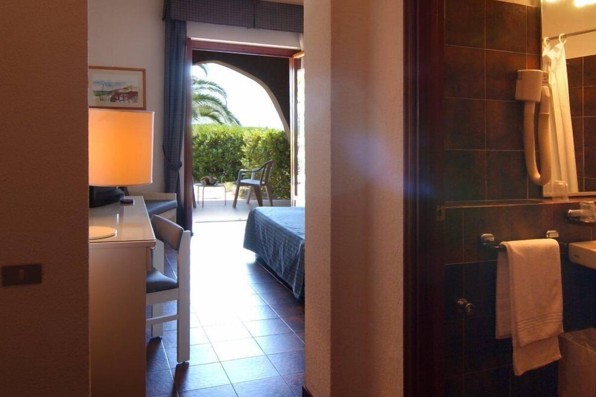 Una camera d'albergo con un letto, una scrivania e una sedia, un bagno con doccia e lavandino, e vista sull'esterno.