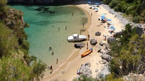A coastal beach with clear turquoise water, rocky terrain, and several boats on the shore. - King's Residence Hotel (Centola)