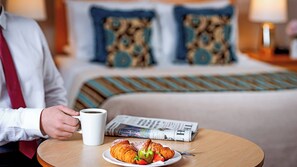 A hotel room with a bed, a bedside table with a newspaper, a coffee cup, and a plate with croissants. - Great National South Court Hotel (Limerick)