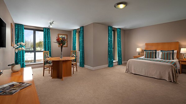Habitación de hotel con cama, escritorio con silla, un jarrón con flores y cortinas color turquesa.