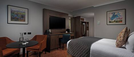 A hotel room with a bed, a desk, a chair, a TV, and two framed artworks.