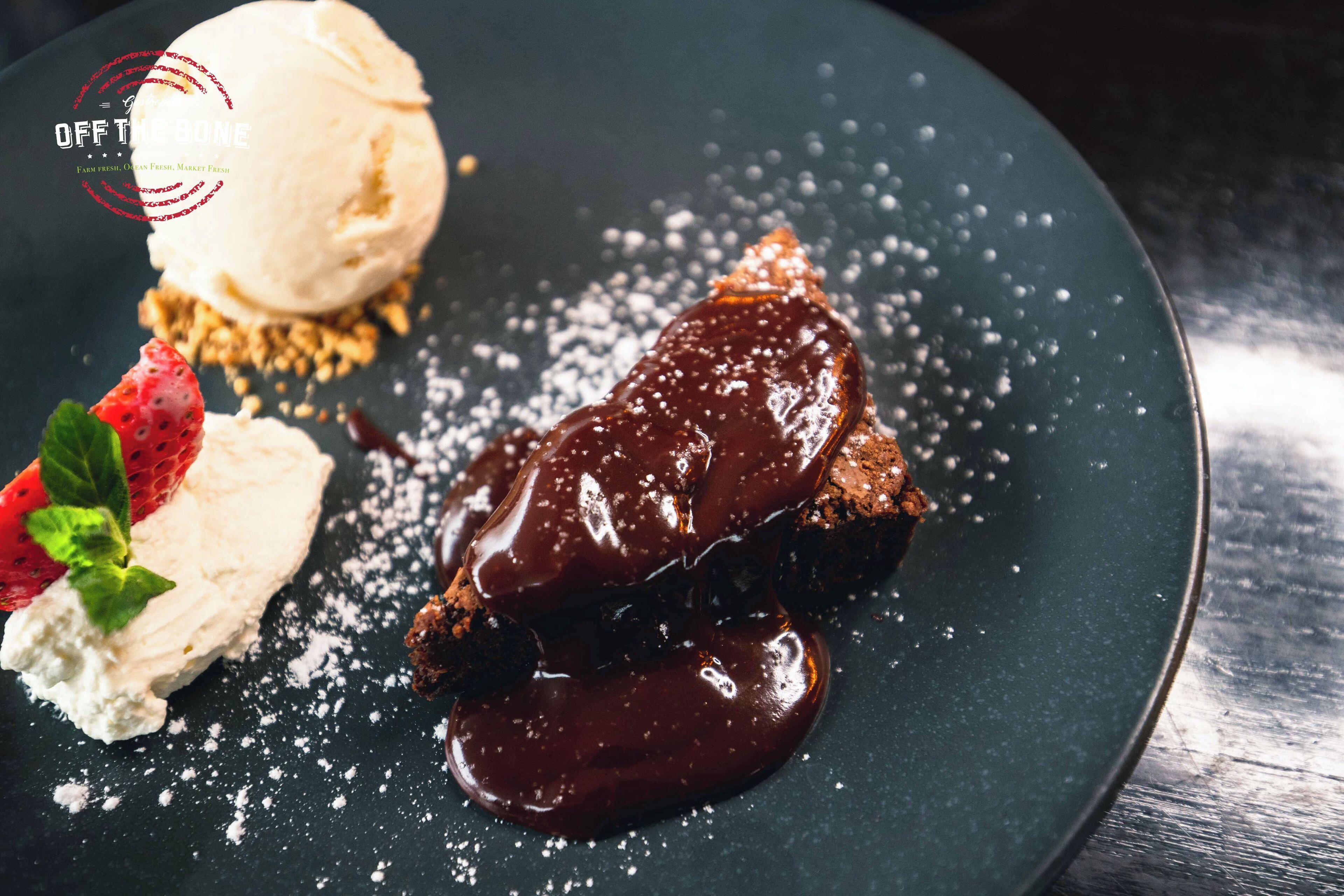 Une assiette de dessert avec une boule de glace à la vanille, un brownie enrobé de chocolat et une fraise en guise de décoration.