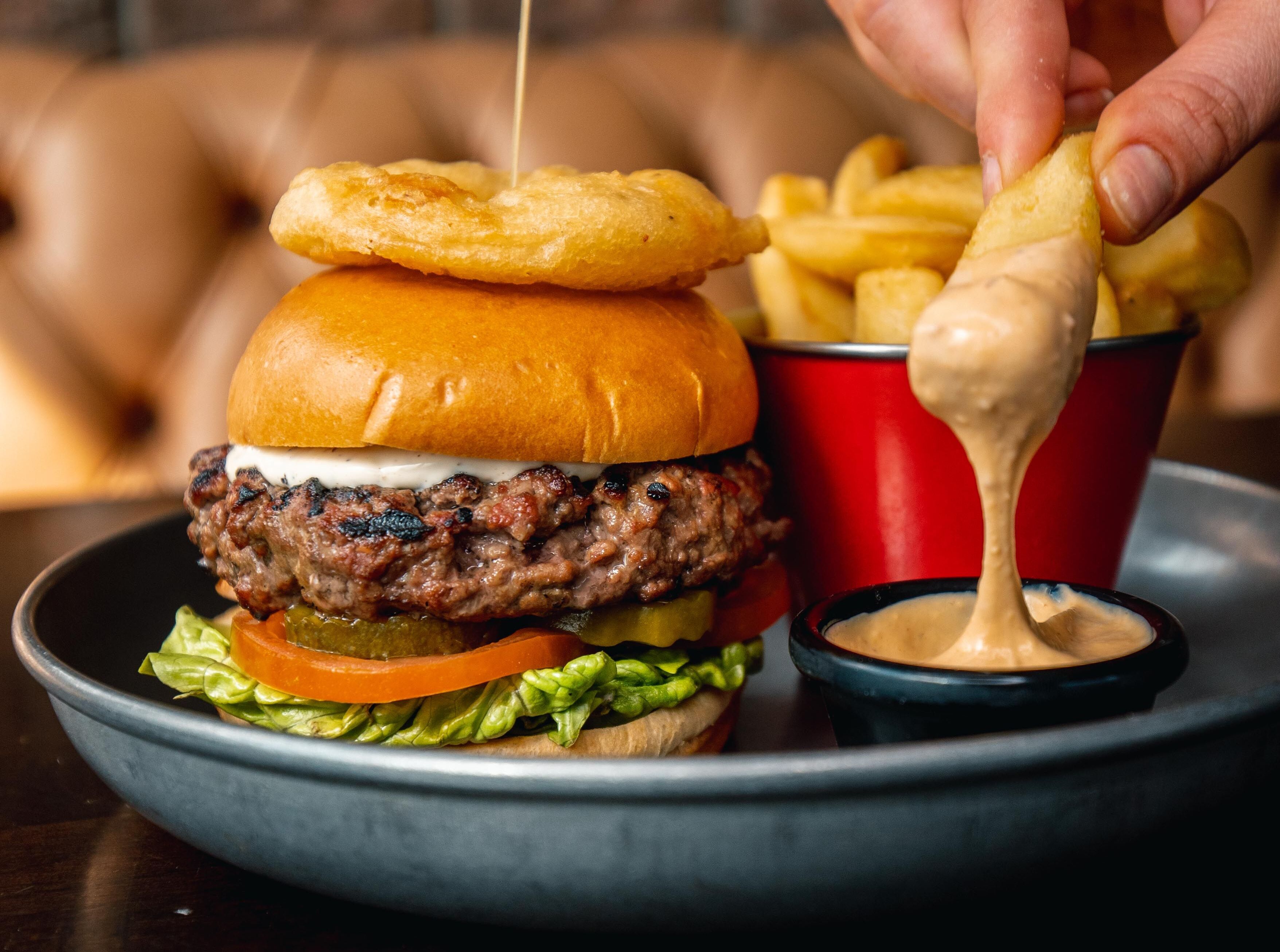 Un hamburger composé d’un pain, d’un steak haché, de fromage, de laitue, de tomates et d’anneaux d’oignon, servi avec des frites et une sauce pour tremper.