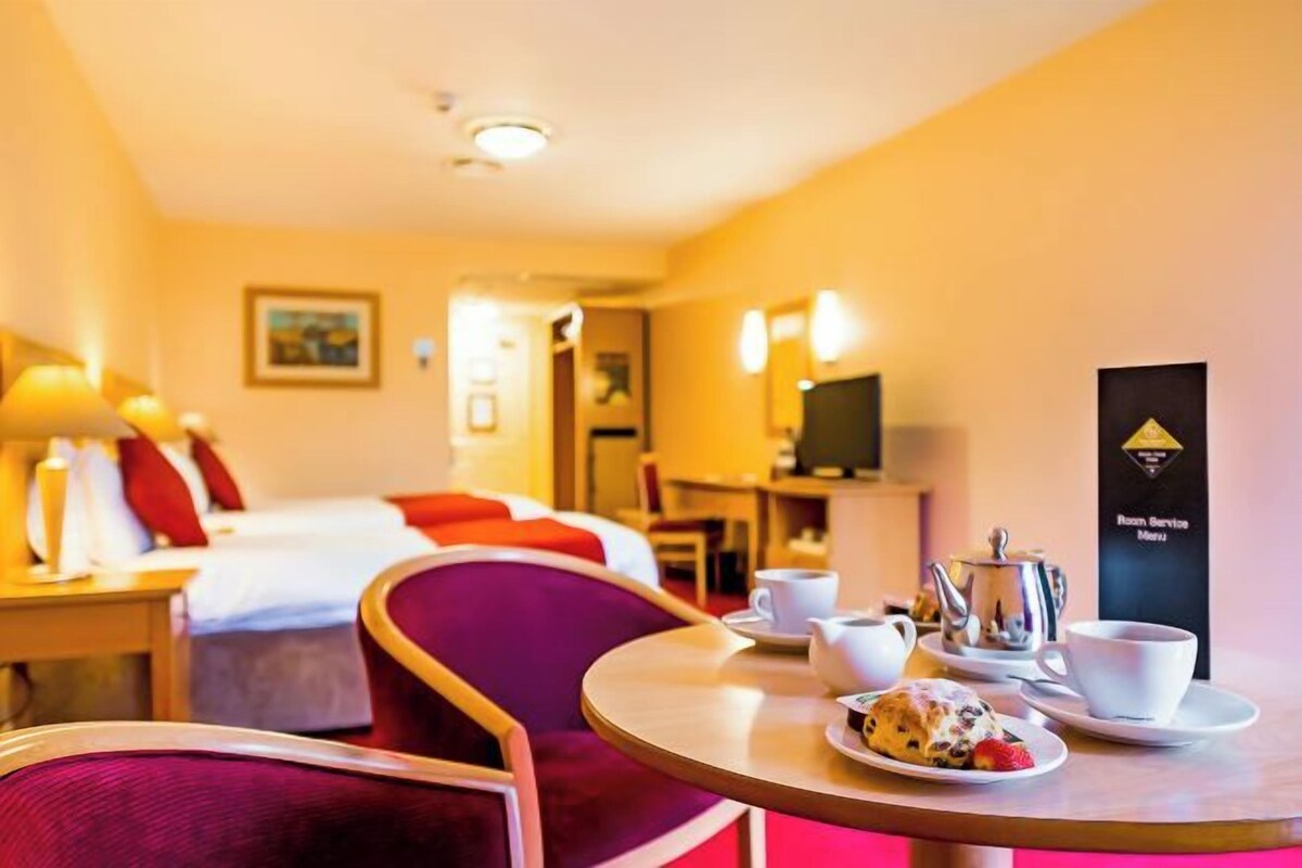 A hotel room with a bed, a dining table with a teapot and cups, and a television.