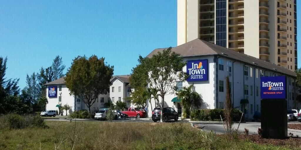 A hotel with multiple signs for InTown Suites and Extended Stay. There are several cars parked in front, and the building is surrounded by trees and other buildings.