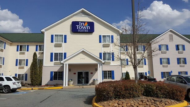 Voici un hôtel dont l’enseigne indique « In Town Suites ». Il se distingue par une entrée centrale avec un porche abrité, de nombreuses fenêtres dotées de volets bleus et un parking avec des places réservées aux personnes handicapées.