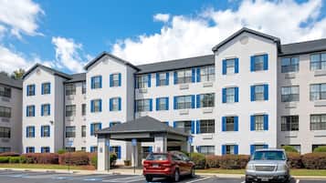 A multi-story hotel with a central entrance, parking spaces, and blue window shutters.