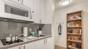 Una cocina moderna con armarios blancos, un microondas, una estufa y un aparador de madera con cestas.