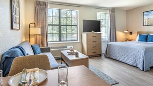 Una habitación de hotel con una cama, un escritorio, un televisor, un sofá y una mesa de comedor con un plato y cubiertos.