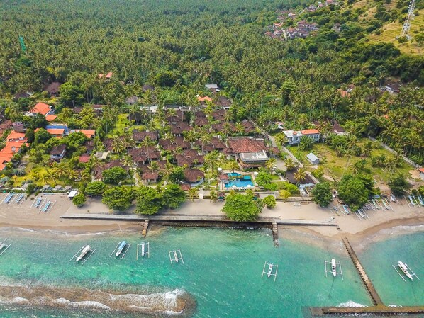 An aerial view of a resort with multiple bungalow-style buildings, a swimming pool, and a beach area with boats.