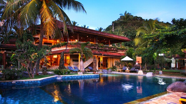 Un resort con piscina, sillas de descanso y una zona cubierta con techo rojo.