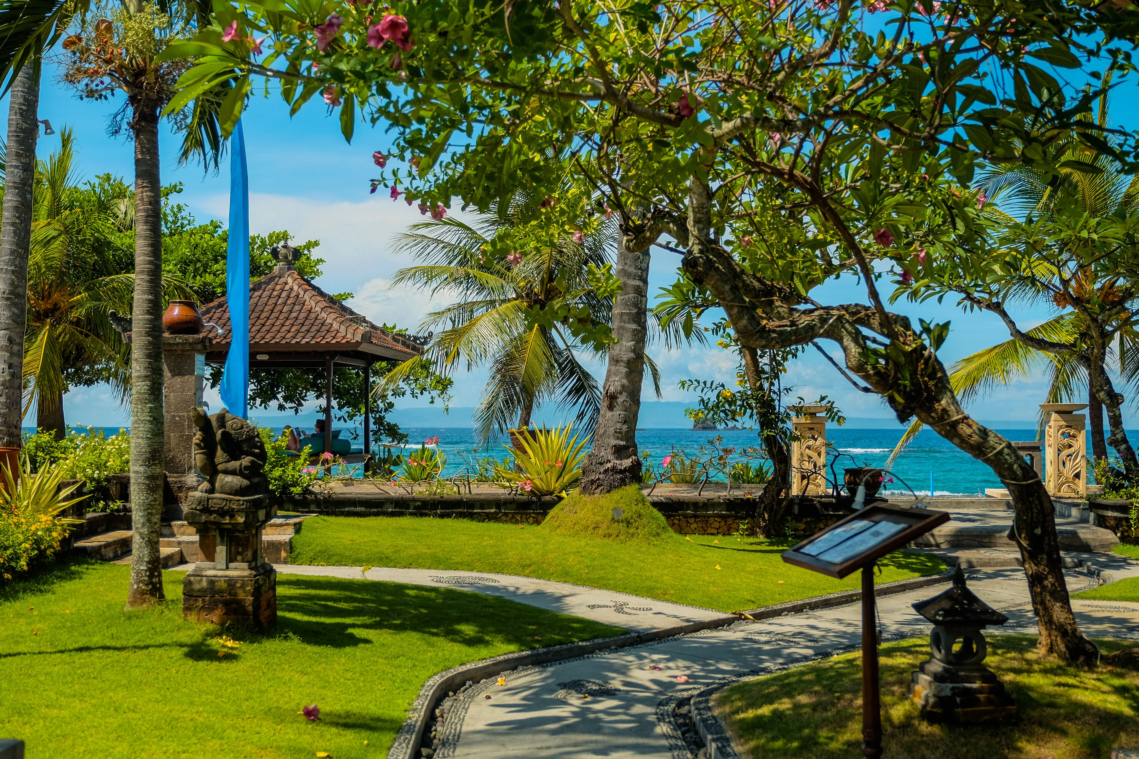 Un giardino tropicale con una statua in pietra, un gazebo e vista sull'oceano.