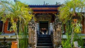 Un edificio tradicional con una escalera que conduce a una puerta, rodeado de palmeras y esculturas de piedra.