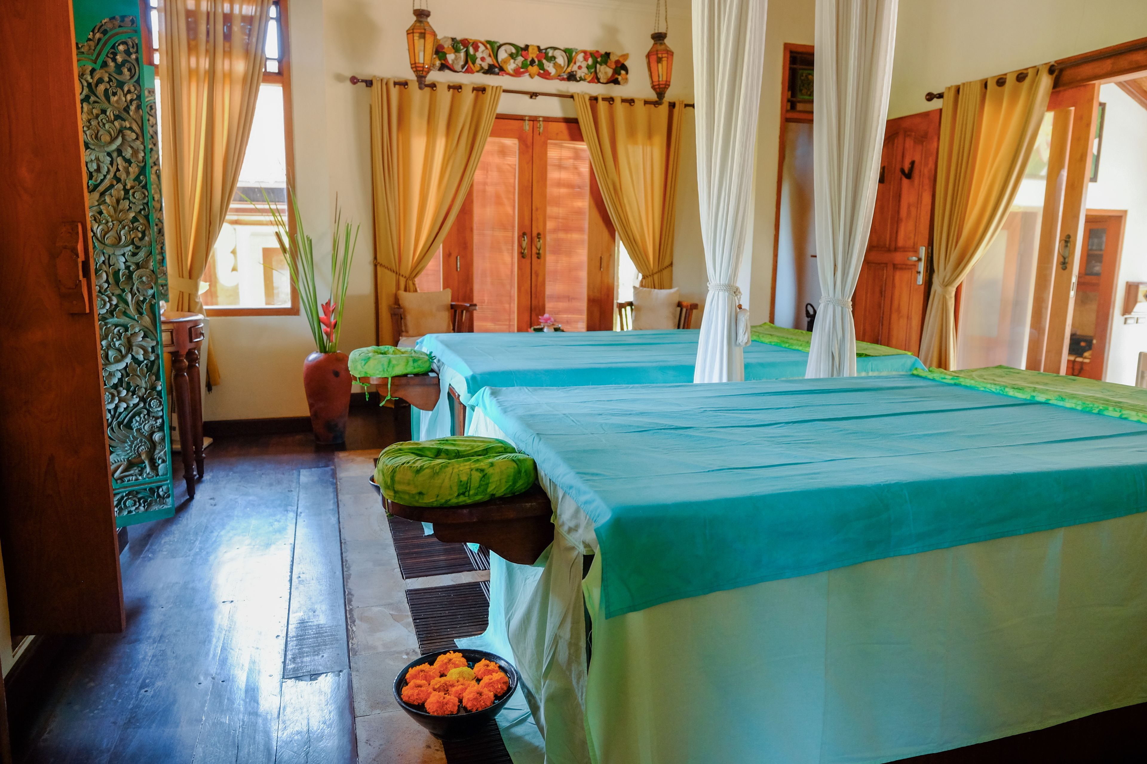 Quarto com duas camas, piso de madeira, janela com cortinas e porta com painel decorativo.