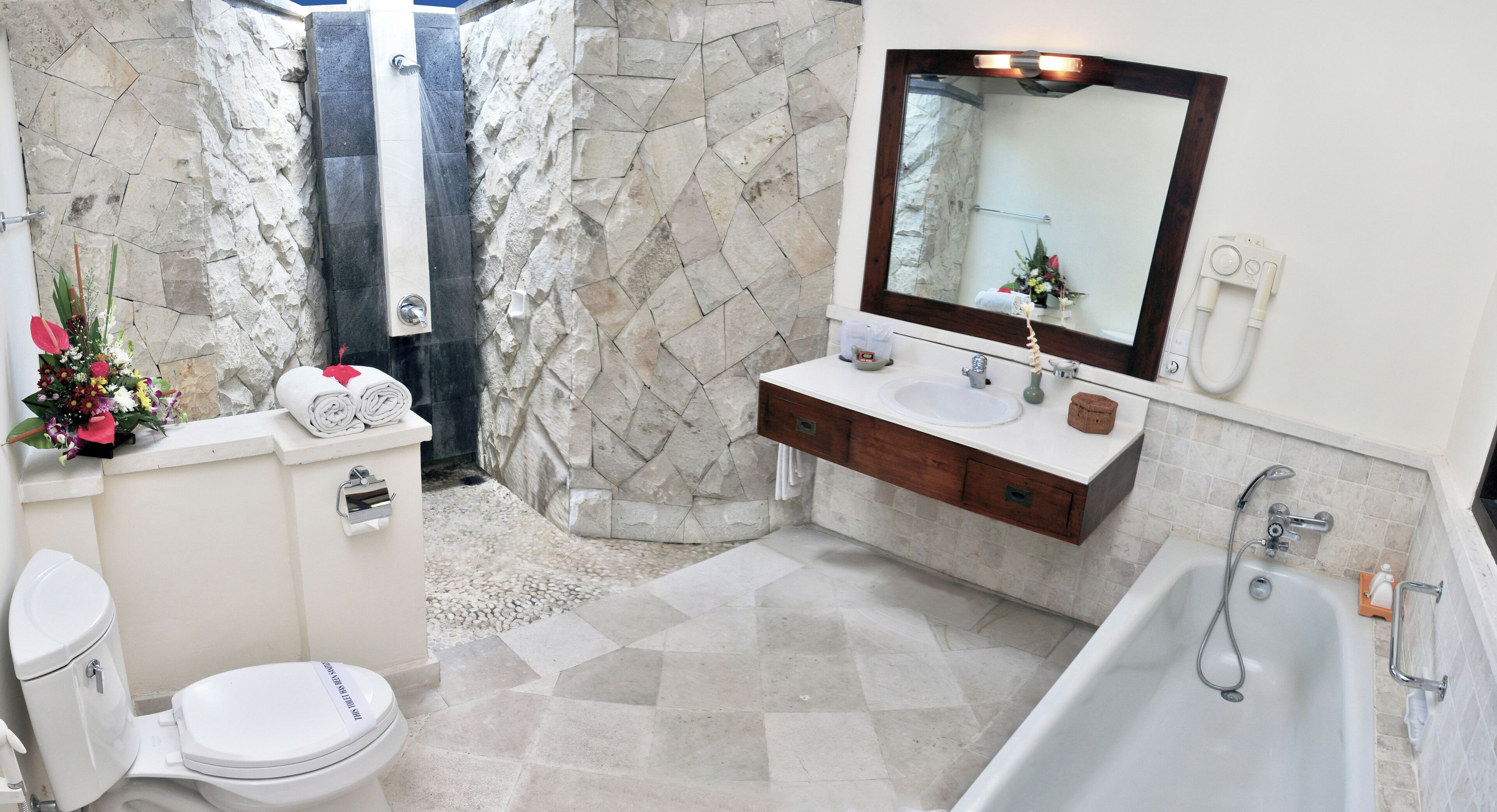 A bathroom with a stone shower, a white toilet, a sink with a mirror, and a bathtub.