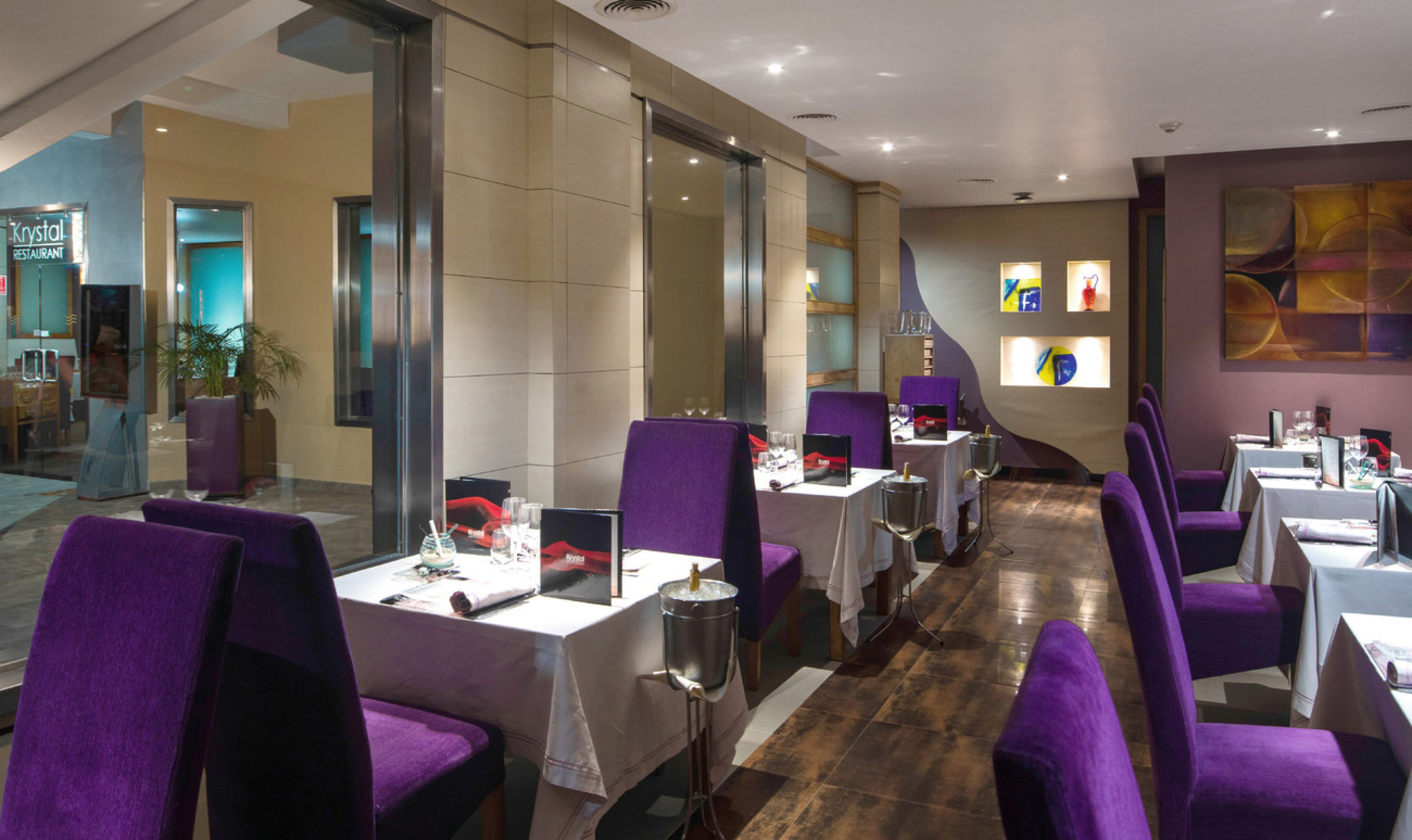 Een restaurant met paarse stoelen en tafels, een glazen wand, en een bordje met de tekst 'Crystal Restaurant'.