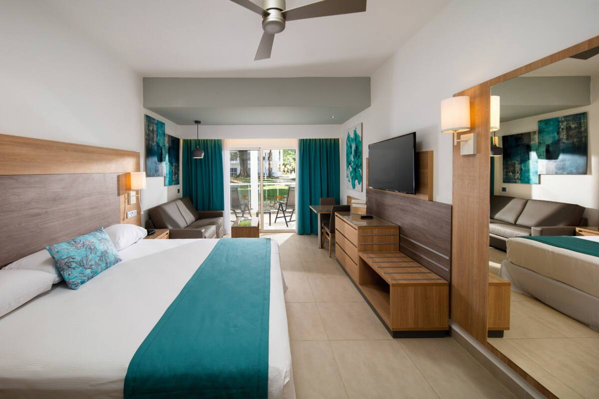 Ein modernes Hotelzimmer mit einem großen Bett, einem Schreibtisch, einem Fernseher und einem Balkon mit Vorhängen.