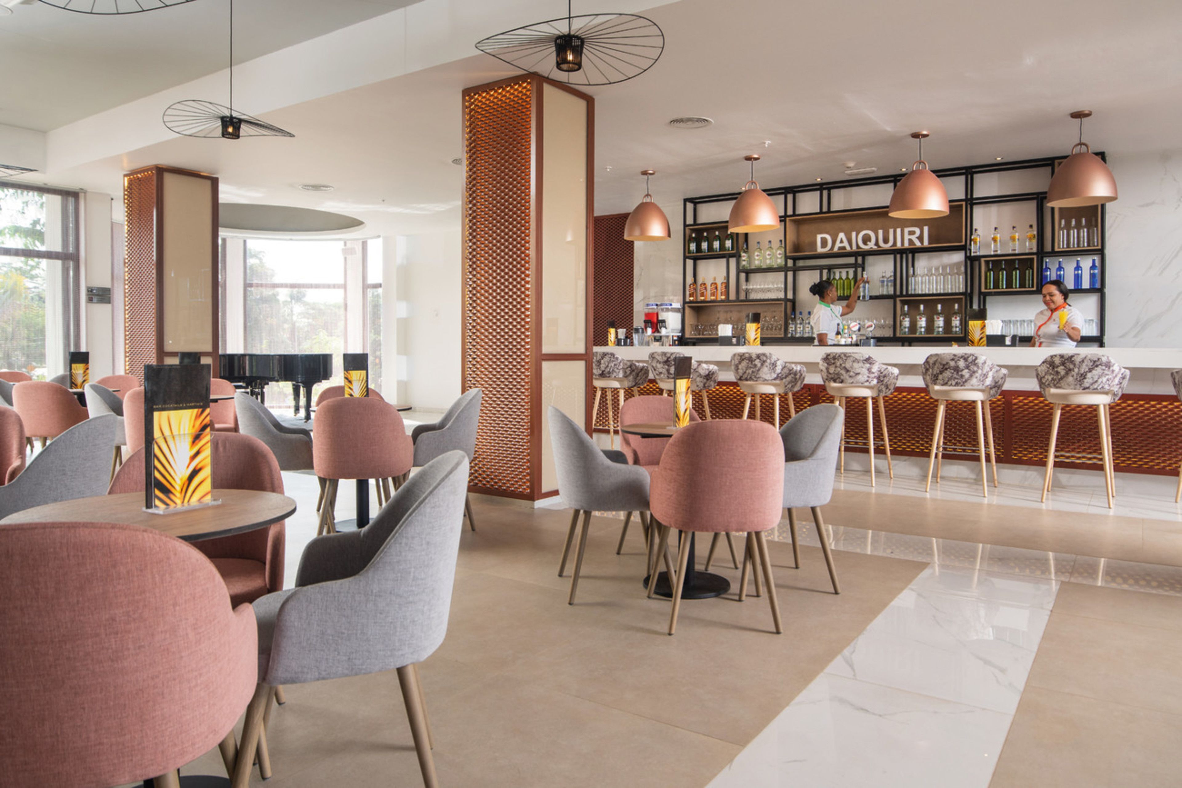 A modern bar area with a Daiquiri sign, seating with grey and pink chairs, and a marble floor.