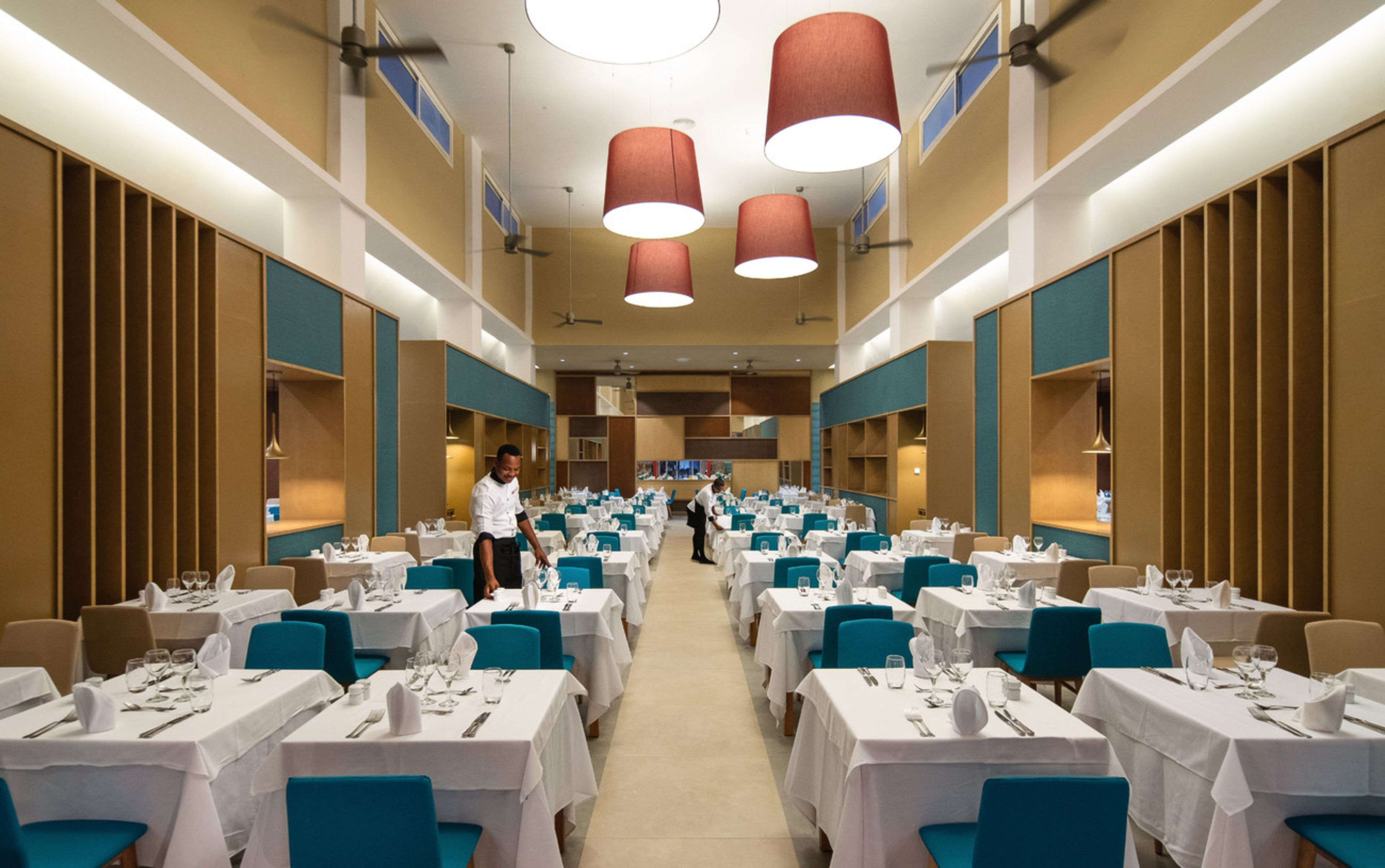A spacious dining area with multiple tables, each set with white tablecloths and blue chairs.