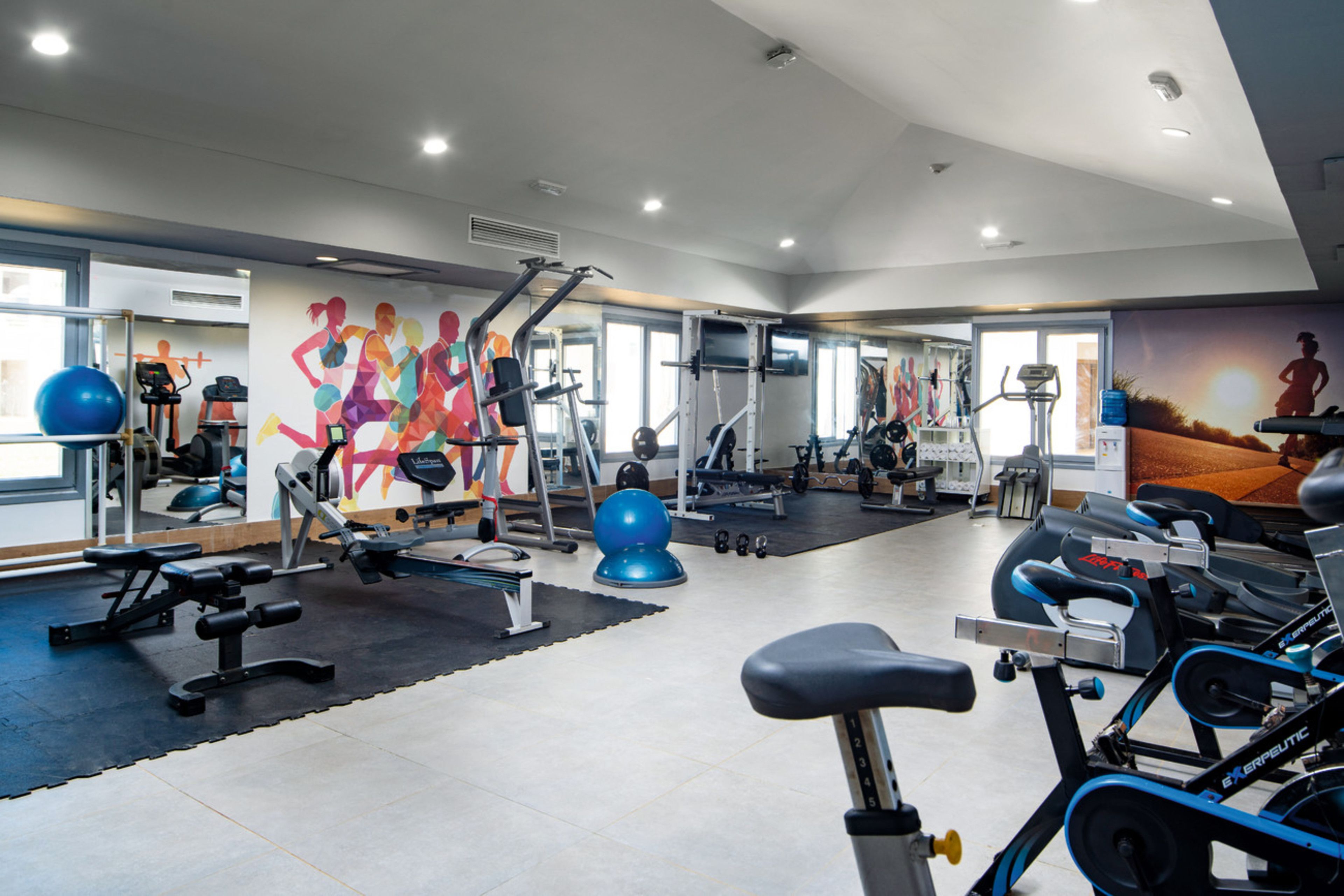 Un gimnasio con equipo de ejercicio, un espejo grande y un mural de corredores.