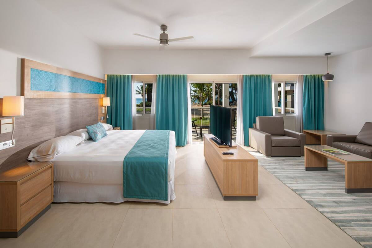 Ein modernes Hotelzimmer mit einem großen Bett, einem Fernseher, einer Couch, einem Schreibtisch und einem Balkon mit Meerblick.
