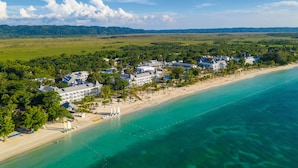 An aerial view of a coastal resort with beachfront villas, a sandy beach, and a clear blue sea. - Hotel Riu Palace Tropical Bay - All Inclusive (Negril)