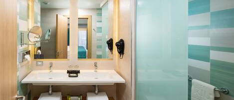 A modern bathroom with two sinks, a mirror, a phone, and a glass shower enclosure.