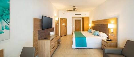 A hotel room with a bed, a TV, a desk, a chair, a sofa, and a ceiling fan.